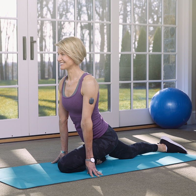 Mujer haciendo una postura de yoga mientras lleva un sistema de MCG Eversense.