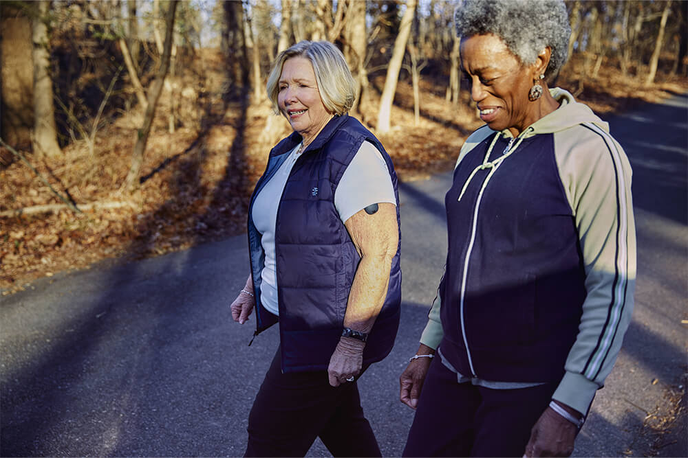 Dos mujeres mayores paseando mientras hablan sobre la cobertura de seguro para el sistema de monitorización continua de la glucosa.