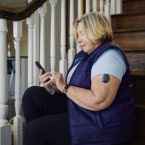 Woman sitting on the stairs while using the Eversense CGM app with her implantable CGM. 